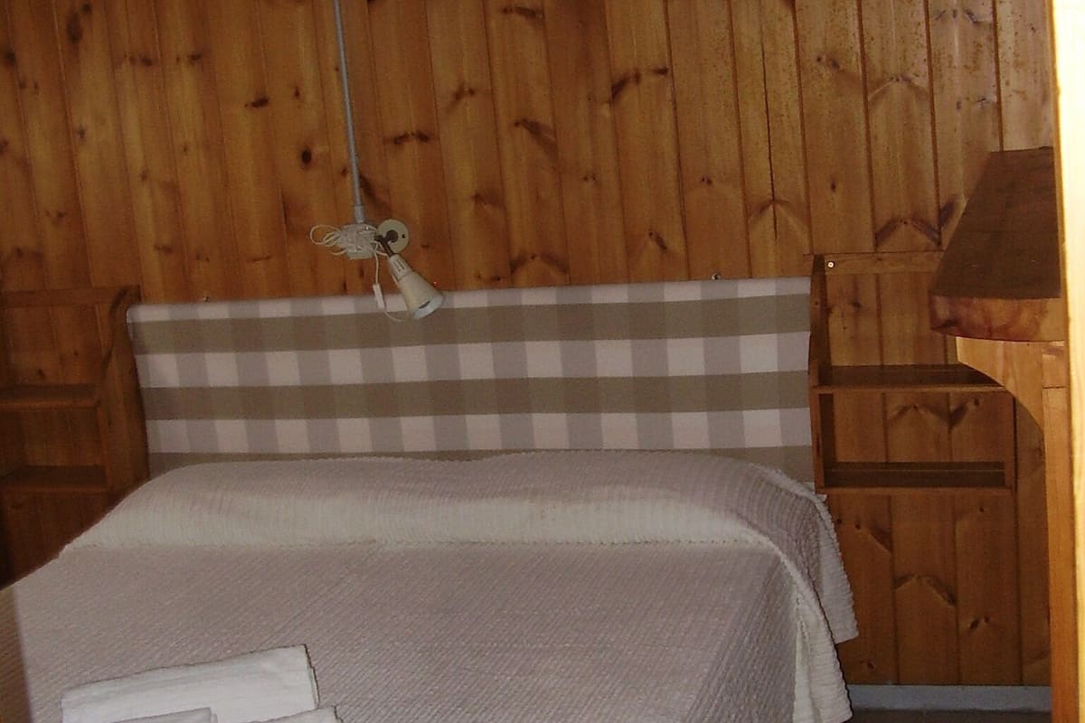 A bedroom with a wooden wall, a checkered headboard, a bed with white bedding, and a nightstand with a lamp.