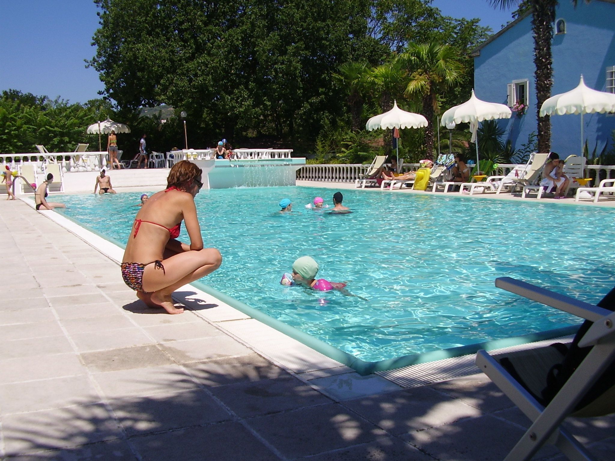 Een zwembad met mensen in het water, ligbedden en parasols.