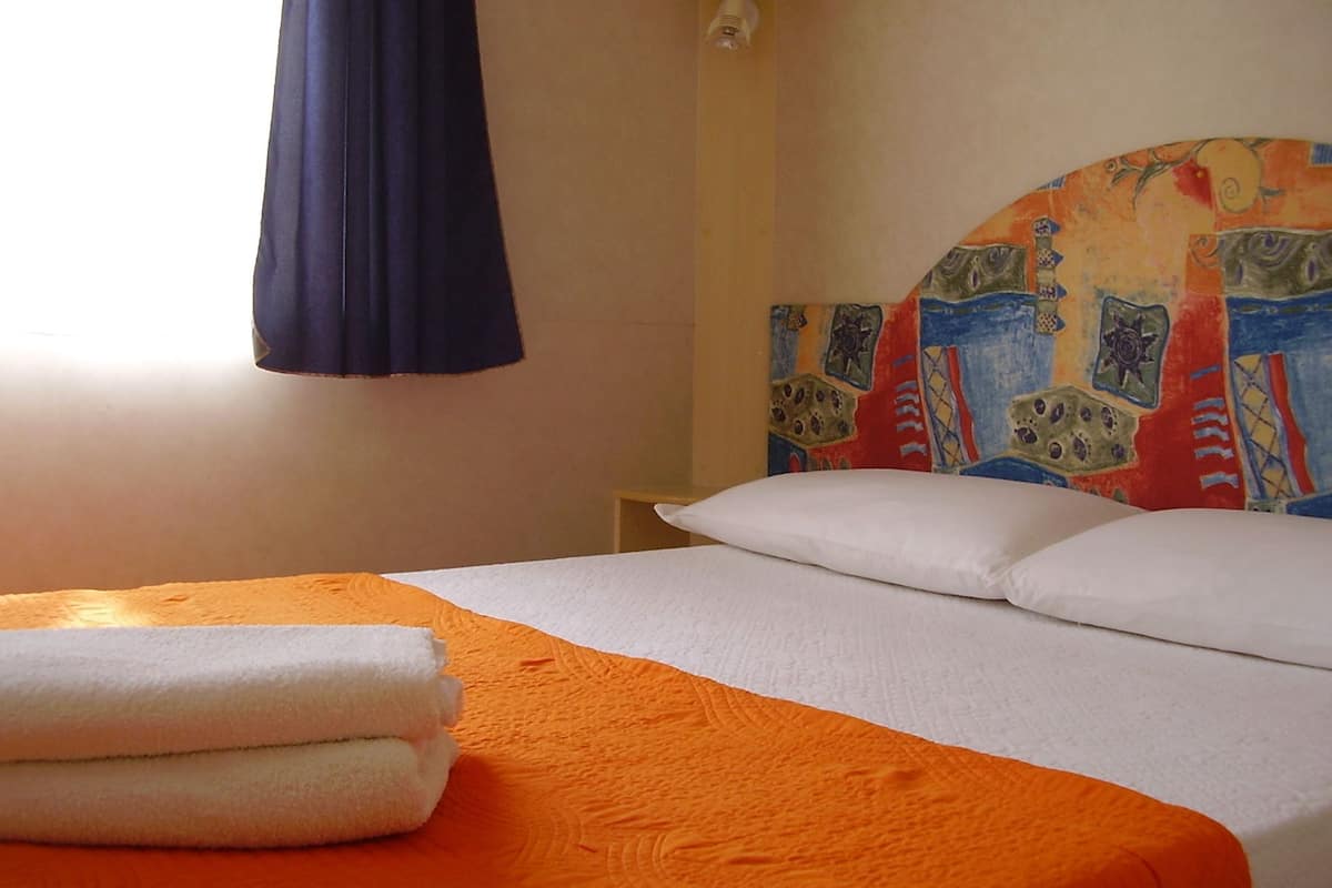 A hotel room with a bed, an orange bedspread, white pillows, and a colorful headboard.