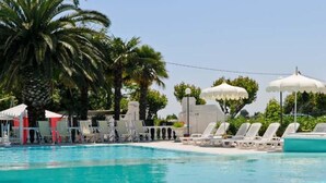 A swimming pool with lounge chairs and umbrellas, surrounded by palm trees. - Camping Village Riviera (Numana)