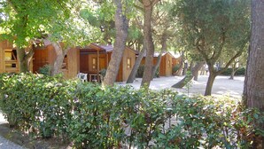 A row of wooden cabins with a gravel path in front, surrounded by dense shrubbery. - Camping Village Riviera (Numana)