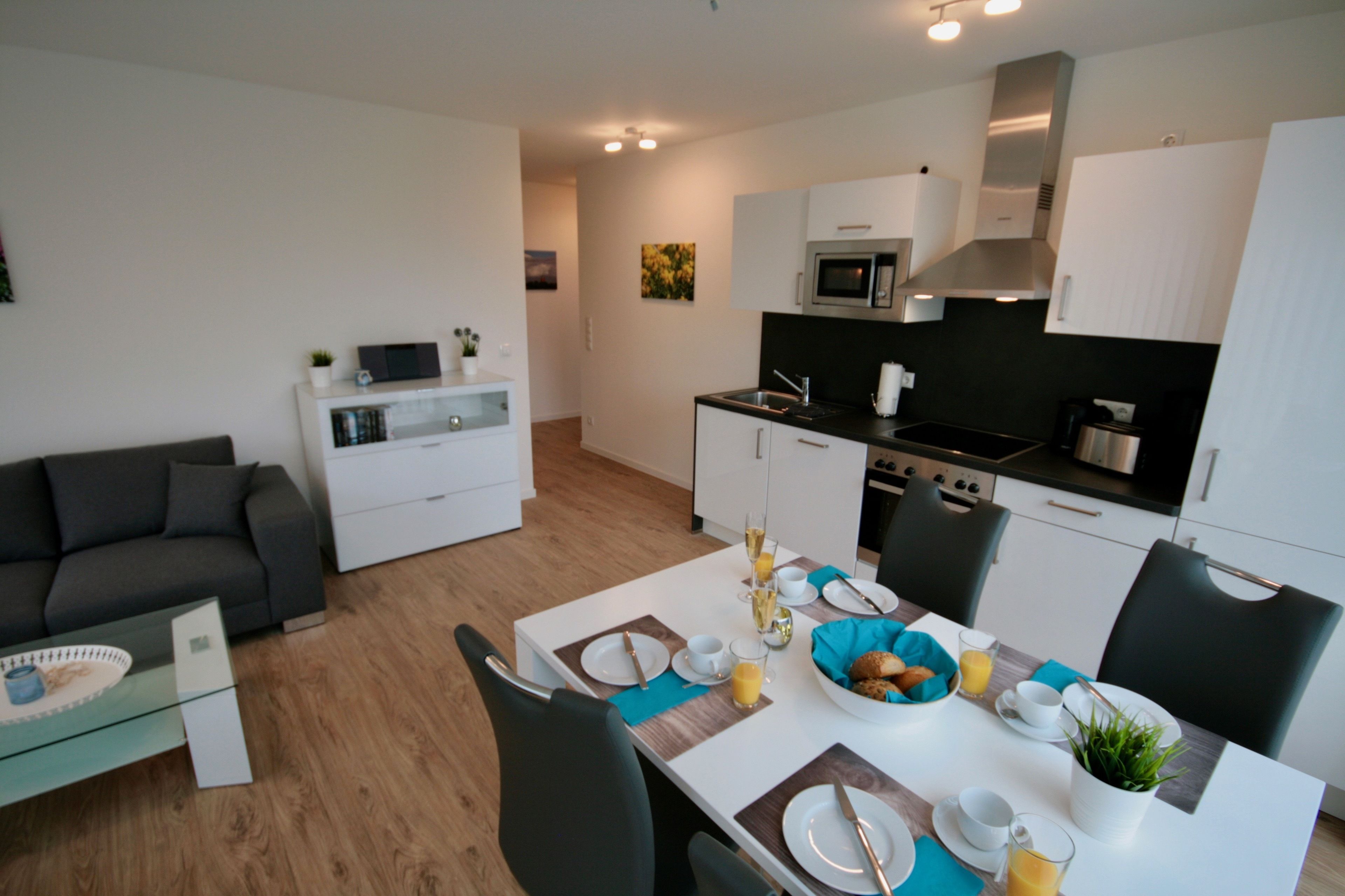 A modern kitchen with white cabinets, a microwave, and a stove. There is a dining table with chairs and a sofa in the living area.