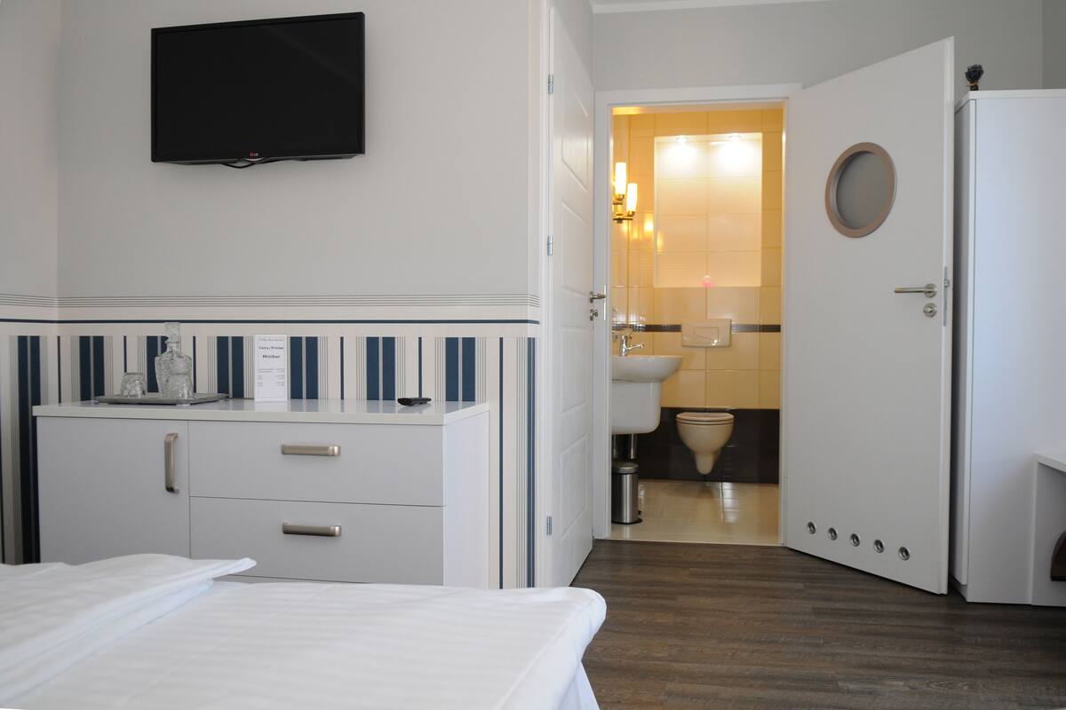 Une chambre d’hôtel équipée d’un lit, d’un minibar, d’une télévision et d’une salle de bain visible à travers une porte ouverte.