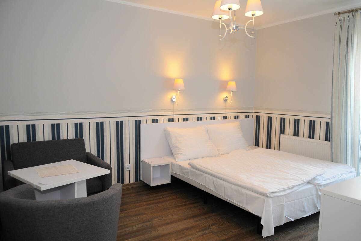 Une chambre d’hôtel avec un lit simple, une petite table, une chaise et deux lampes fixées au mur.
