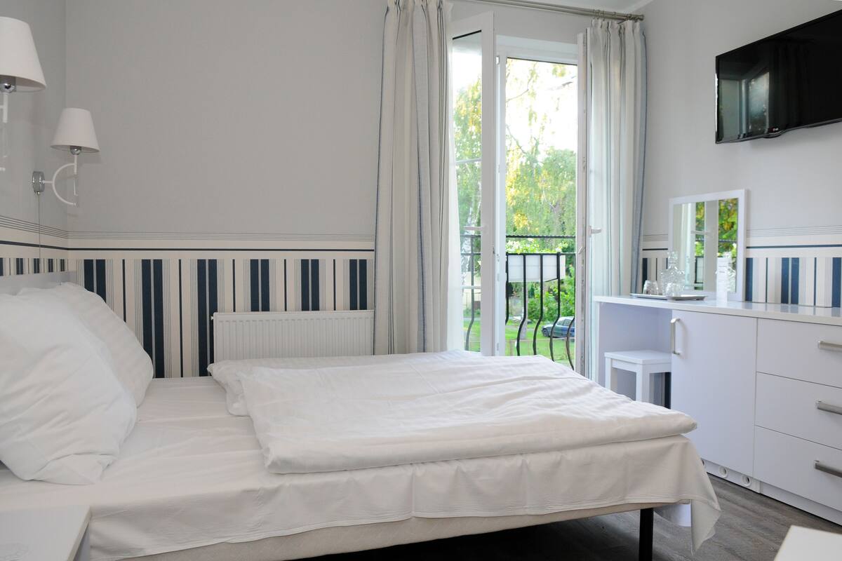 Une chambre à coucher comprenant un lit, une table de chevet, une commode, un miroir et un téléviseur fixé au mur.