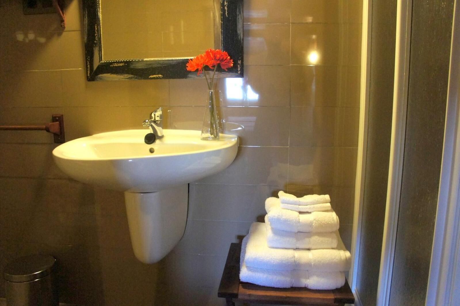 A bathroom with a sink, mirror, and a stack of white towels on a wooden shelf.