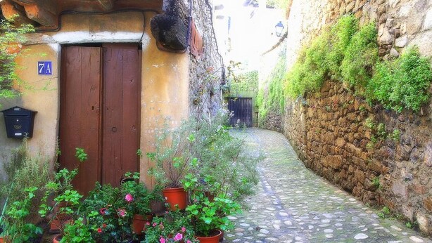 A narrow cobblestone alley with a rustic stone wall on one side and a wooden door with a number '7A' sign. - Casa Rural Estrela (San Martin de Trevejo)