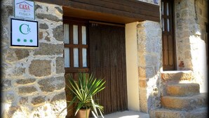 A stone building with a wooden door and a potted plant in front. There are signs indicating a hotel named "CASA ESTRELA" and a rating of "CR". - Casa Rural Estrela (San Martin de Trevejo)