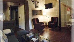 A living room with two armchairs, a sofa, a coffee table, and a flat-screen TV mounted on the wall. - Casa Rural Estrela (San Martin de Trevejo)