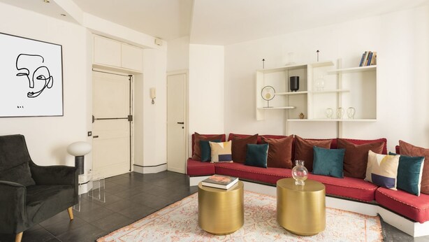 A modern living room with a red sofa, two gold side tables, a black armchair, and a patterned rug. - Lively 1BR in Monti by Sonder (Rome)