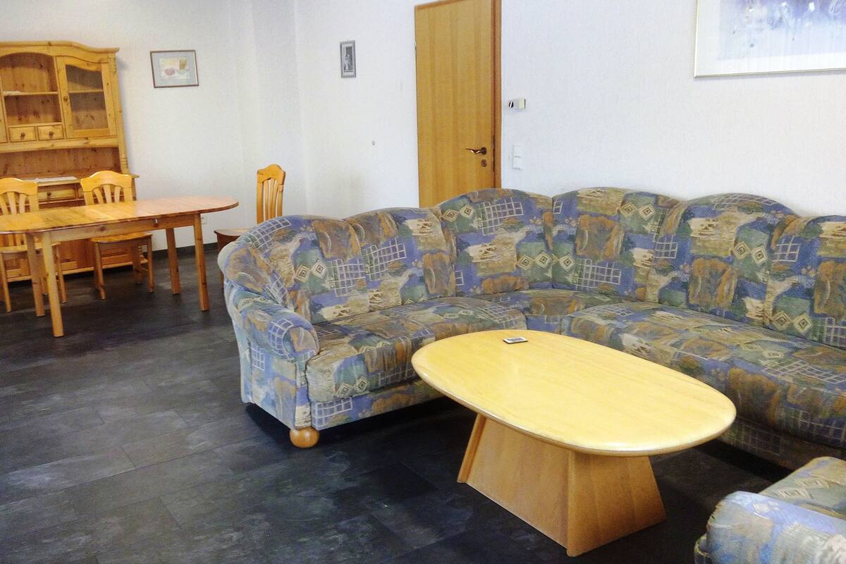 Ein Wohnzimmer mit einer gemusterten Couch, einem Holzesstisch mit Stühlen und einem Schrank.