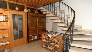 Een houten trap met metalen leuning, een houten boekenkast vol boeken, en een houten kast met glazen deur.