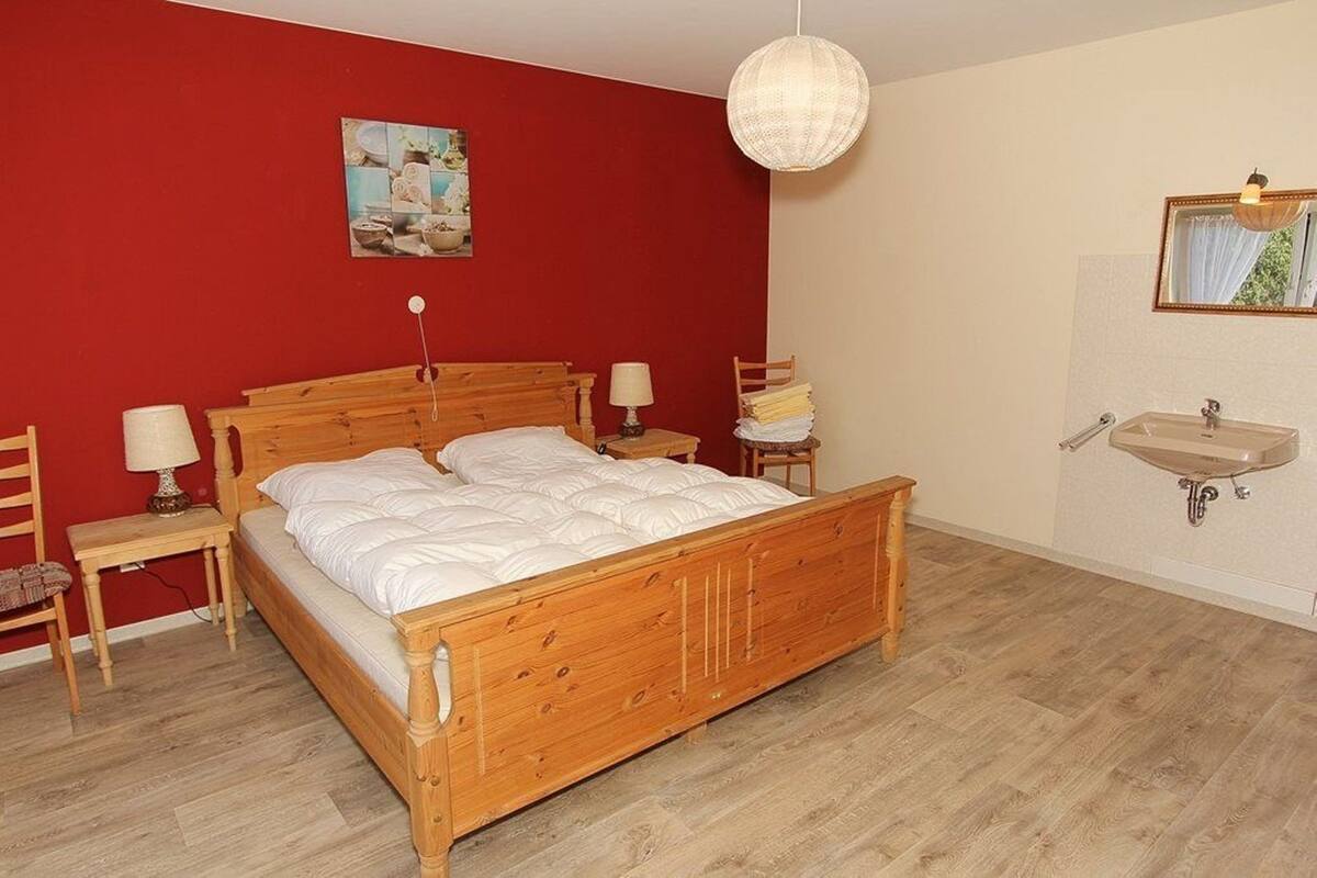 Ein Schlafzimmer mit einem hölzernen Bett, Nachttischen, einer Pendelleuchte, einem wandmontierten Waschbecken und einem Gemälde.
