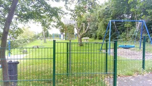 Een omheind park met een schommel, een picknicktafel en een speelplaats.