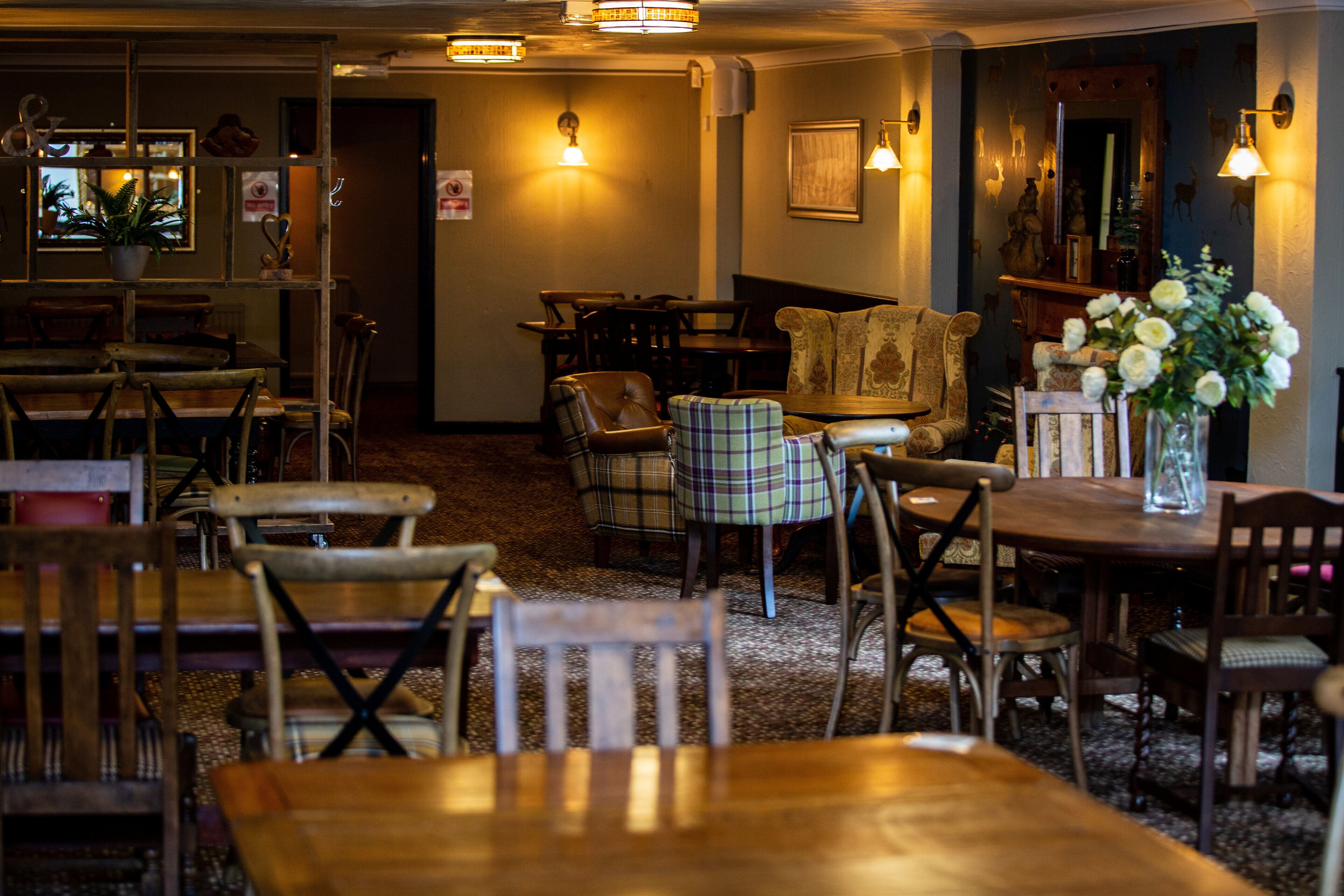 A cozy restaurant with wooden furniture, a variety of seating options including tables and chairs, and warm lighting.