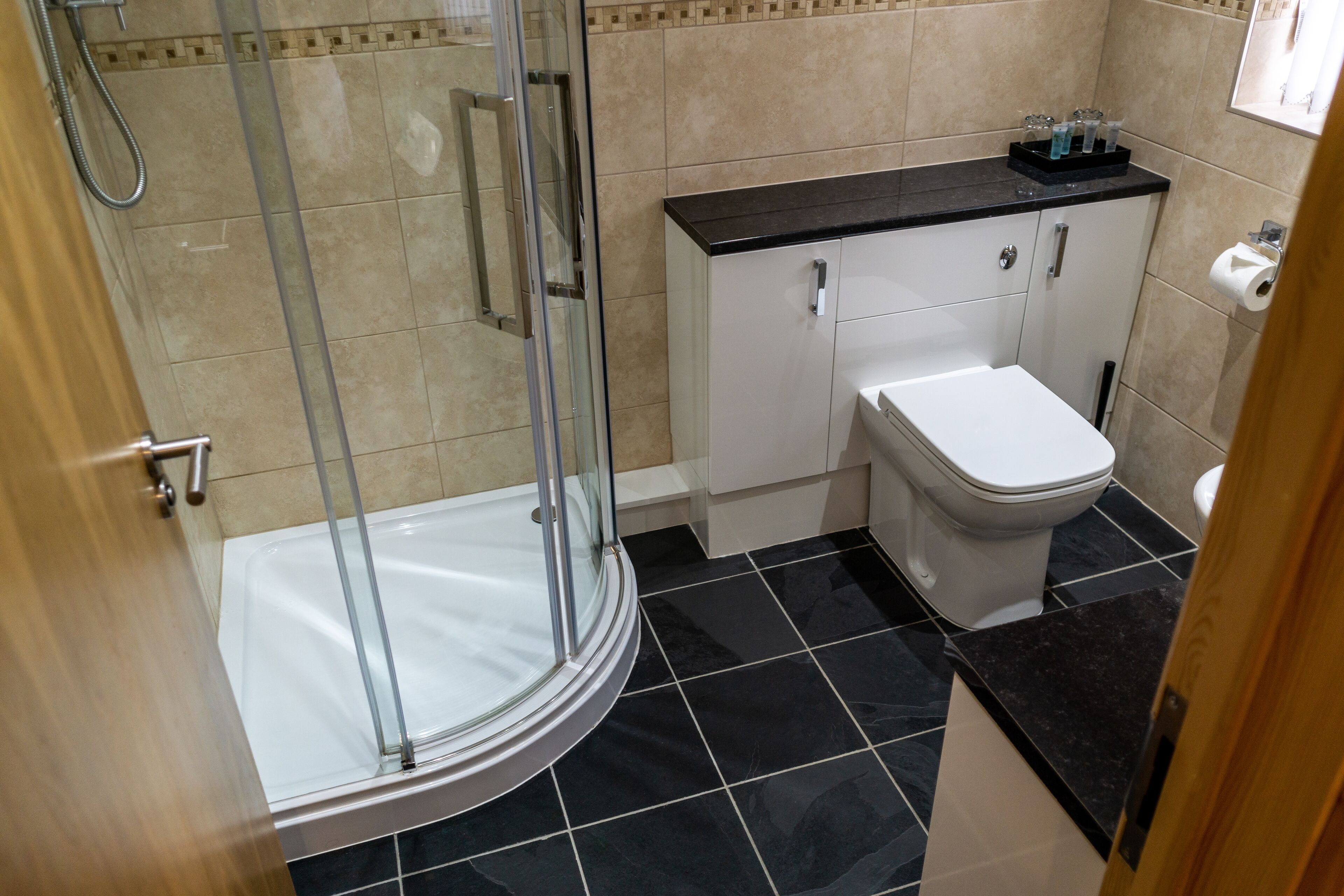 Een moderne badkamer met een douchecabine van glas, een wit toilet en een zwart aanrecht met kastjes.