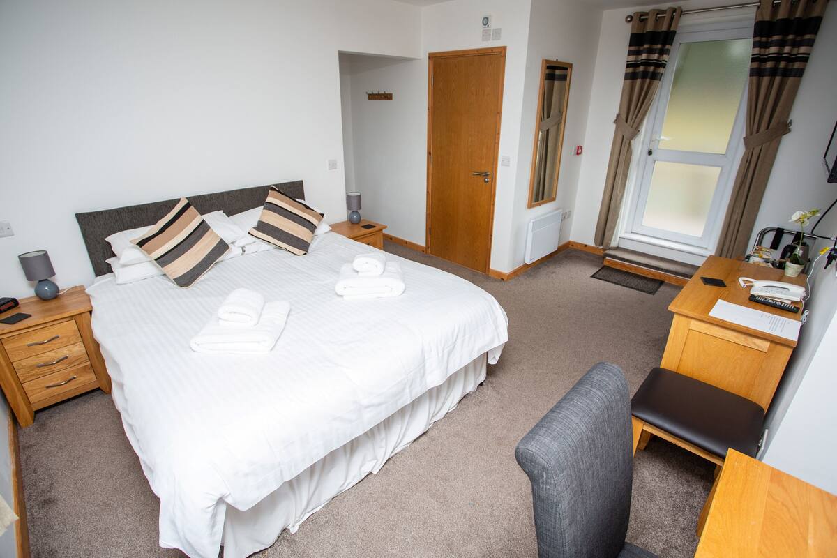 A neatly arranged hotel room with a large bed, bedside tables, a desk, and a chair.