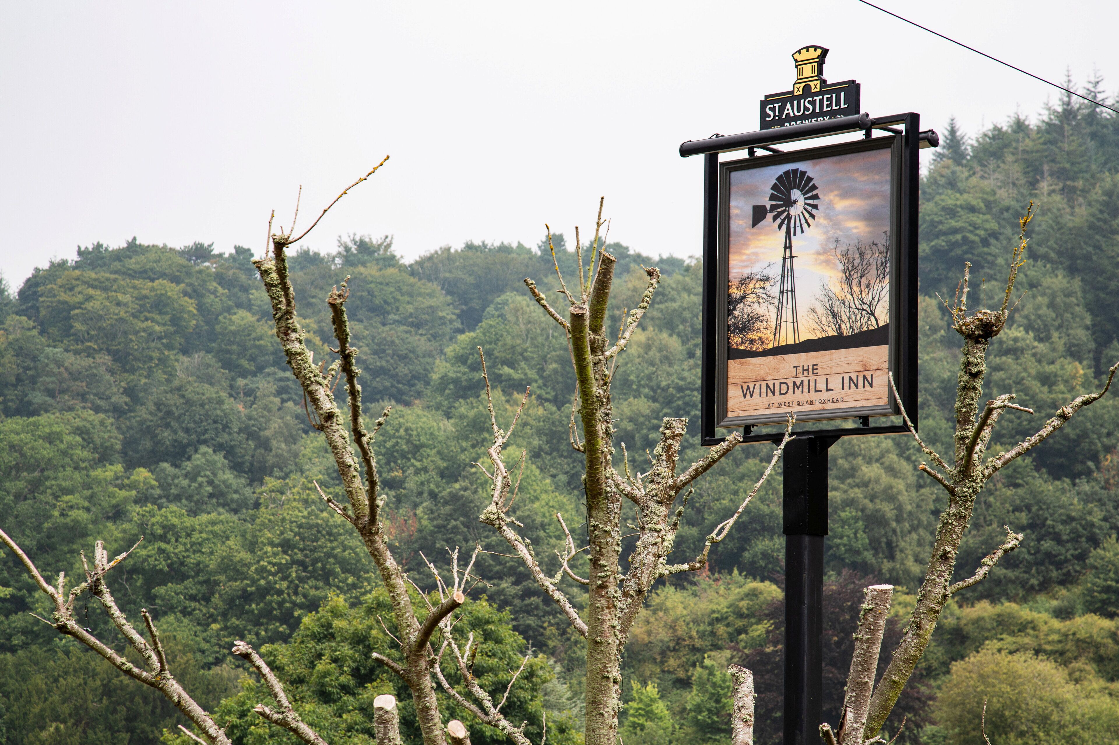 A sign for The Windmill Inn with a windmill illustration, surrounded by trees.