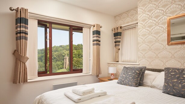 Un dormitorio con una cama grande, una ventana con cortinas, una mesita de noche con lámpara y un espejo en la pared.