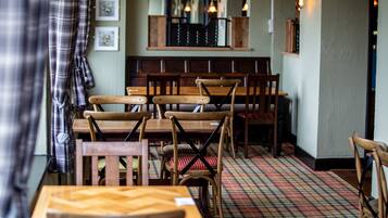 A restaurant interior with wooden tables and chairs, a checkered floor, and a counter with a mirror and hanging lights.