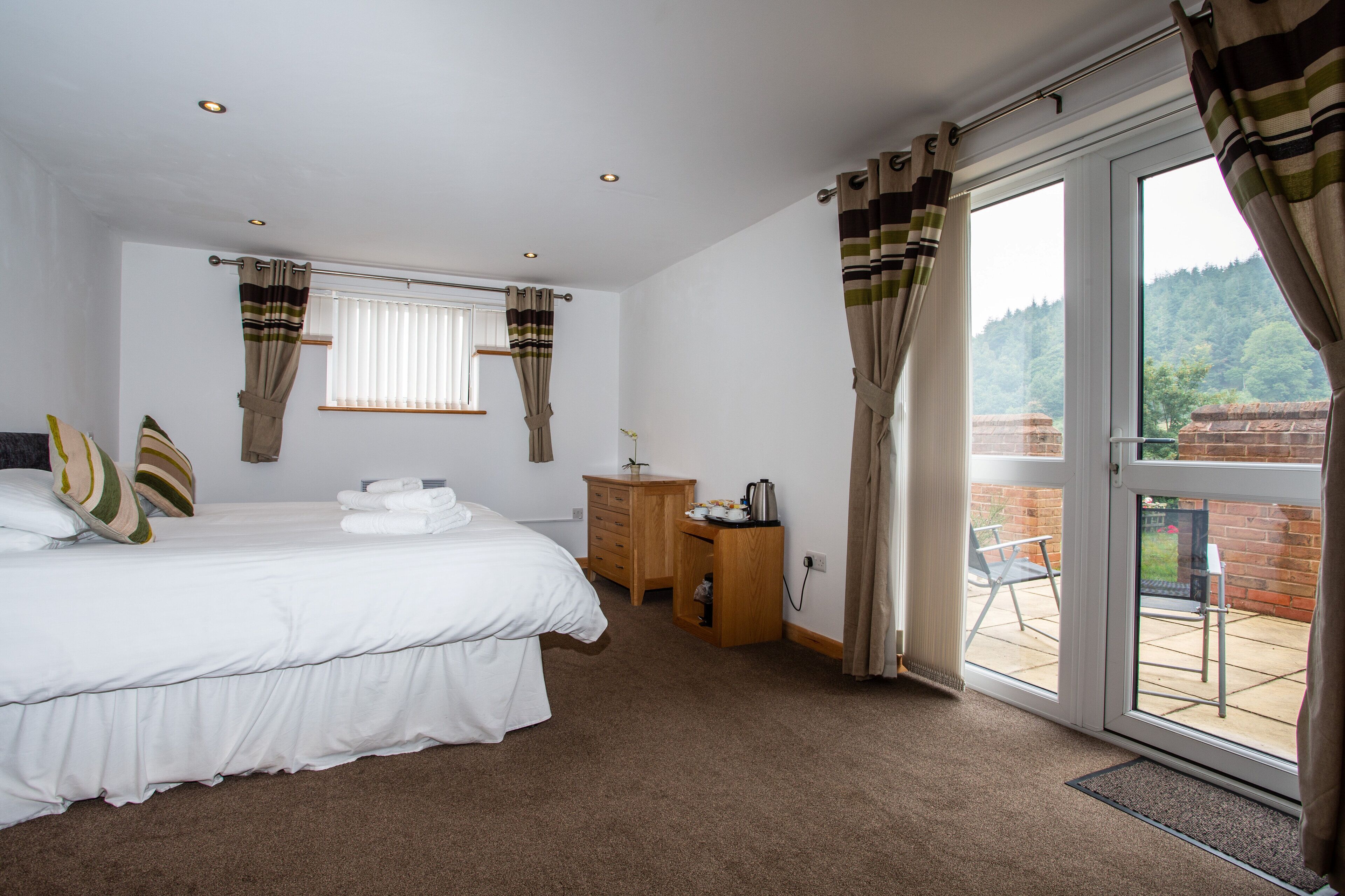 A bedroom with a bed, a wooden dresser, a desk, and a view of the outdoors through a glass door.