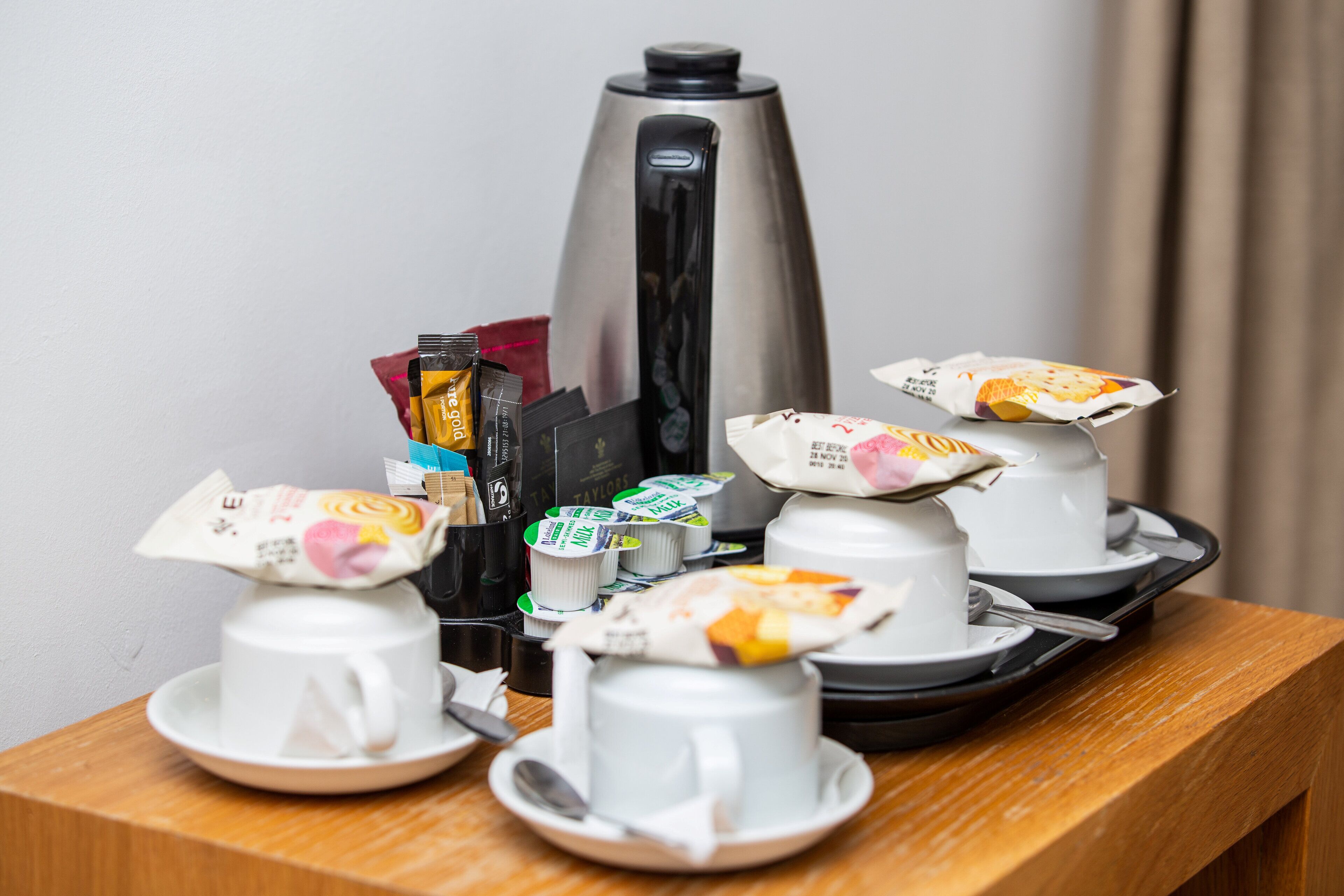 Colazione con macchina del caffè, bustine di tè e alimenti confezionati su un tavolo di legno.