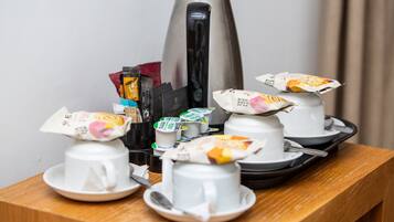 Colazione con macchina del caffè, bustine di tè e alimenti confezionati su un tavolo di legno.