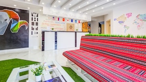 Un moderno vestíbulo de hotel con mostrador de recepción, un llamativo cuadro abstracto en la pared, un sofá rojo con estampado y un mapa mundial.