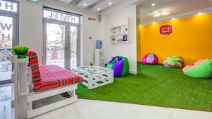 Un moderno vestíbulo de hotel con un sofá rojo y blanco, una mesa de centro de vidrio y coloridos pufs sobre césped artificial.