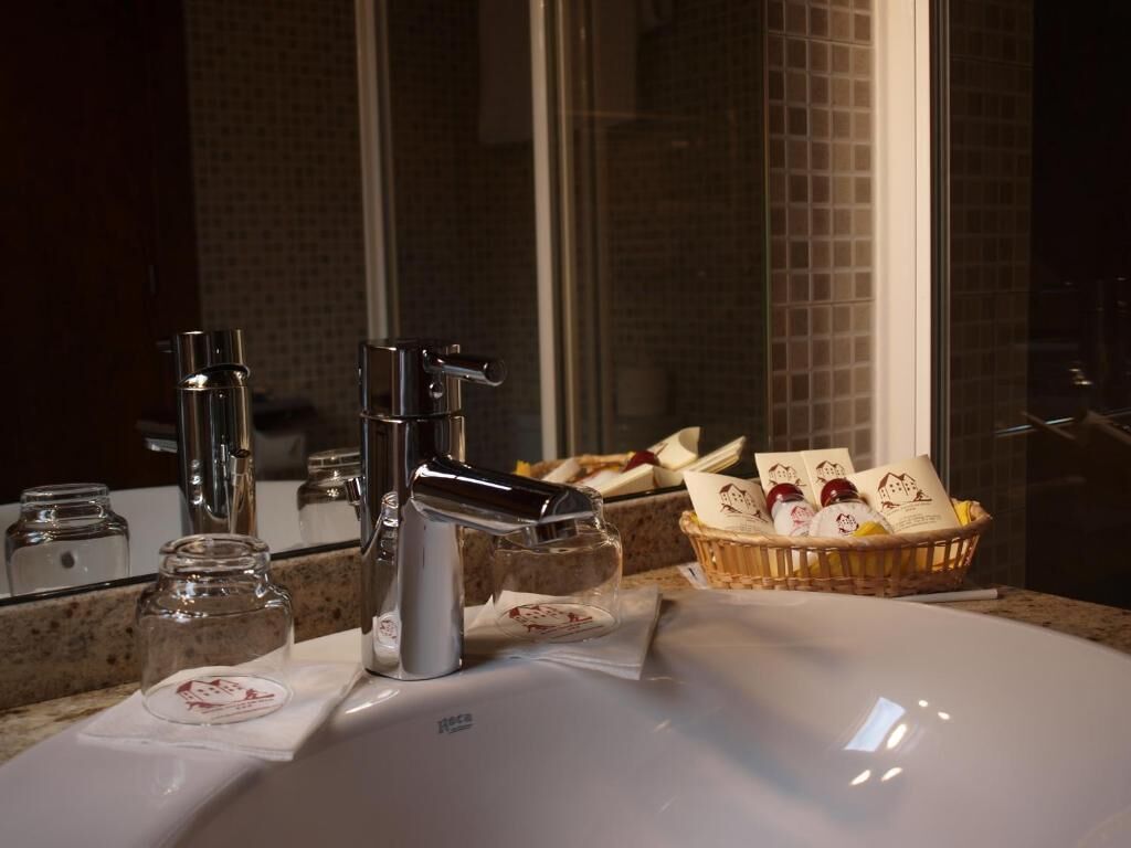 A bathroom with a white sink, two faucets, a mirror, and a basket of toiletries.