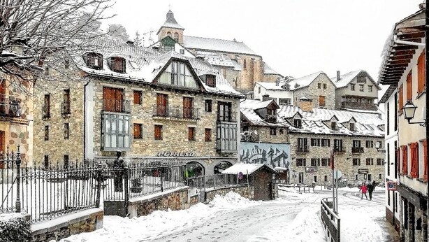 A snow-covered street with historic stone buildings, a small bridge, and a sign for a hotel. - Hotel Valle De Izas (Sallent de Gallego)