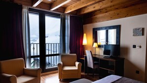 A hotel room with a wooden ceiling, a balcony with curtains, a bed, a desk with a TV, and a chair. - Hotel Valle De Izas (Sallent de Gallego)