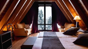 A cozy attic bedroom with a large window, wooden beams, a bed, two chairs, and a desk. - Hotel Valle De Izas (Sallent de Gallego)