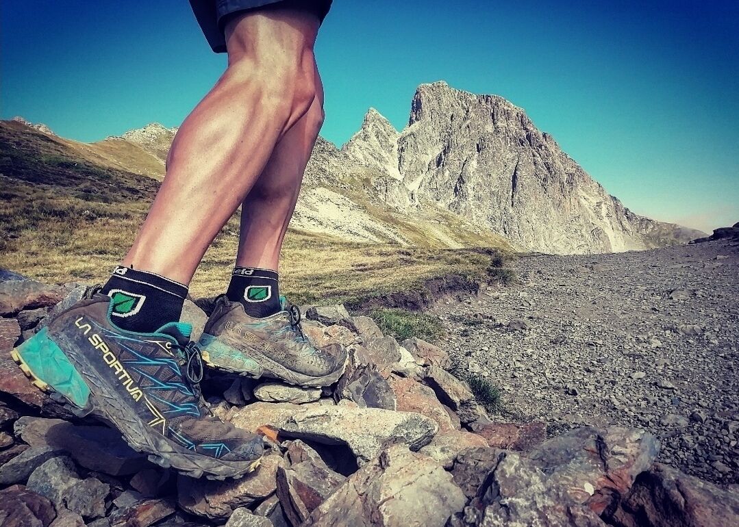 Un par de botas de senderismo sobre terreno rocoso, con una montaña al fondo.
