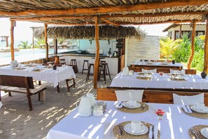 A beachside restaurant with outdoor seating, white tablecloths, and a thatched roof. - Preabeach Villas (Cruz)