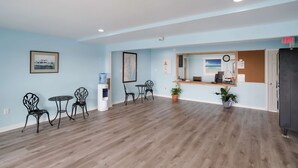 A spacious room with light blue walls, wooden flooring, and a reception desk with a mirror. There are two tables with chairs and a water dispenser. - Rodeway Inn at Somers Cove Marina (Crisfield)