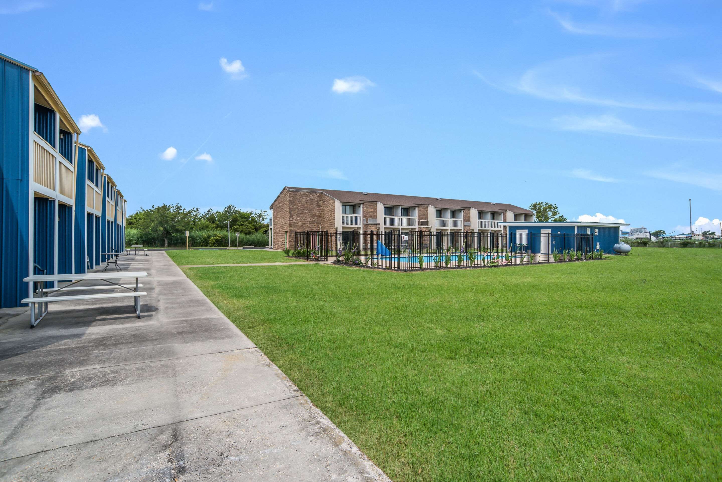 A building with a swimming pool, a grassy area, and a concrete walkway with benches.