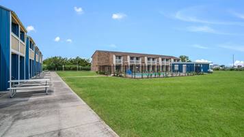 A building with a swimming pool, a grassy area, and a concrete walkway with benches.