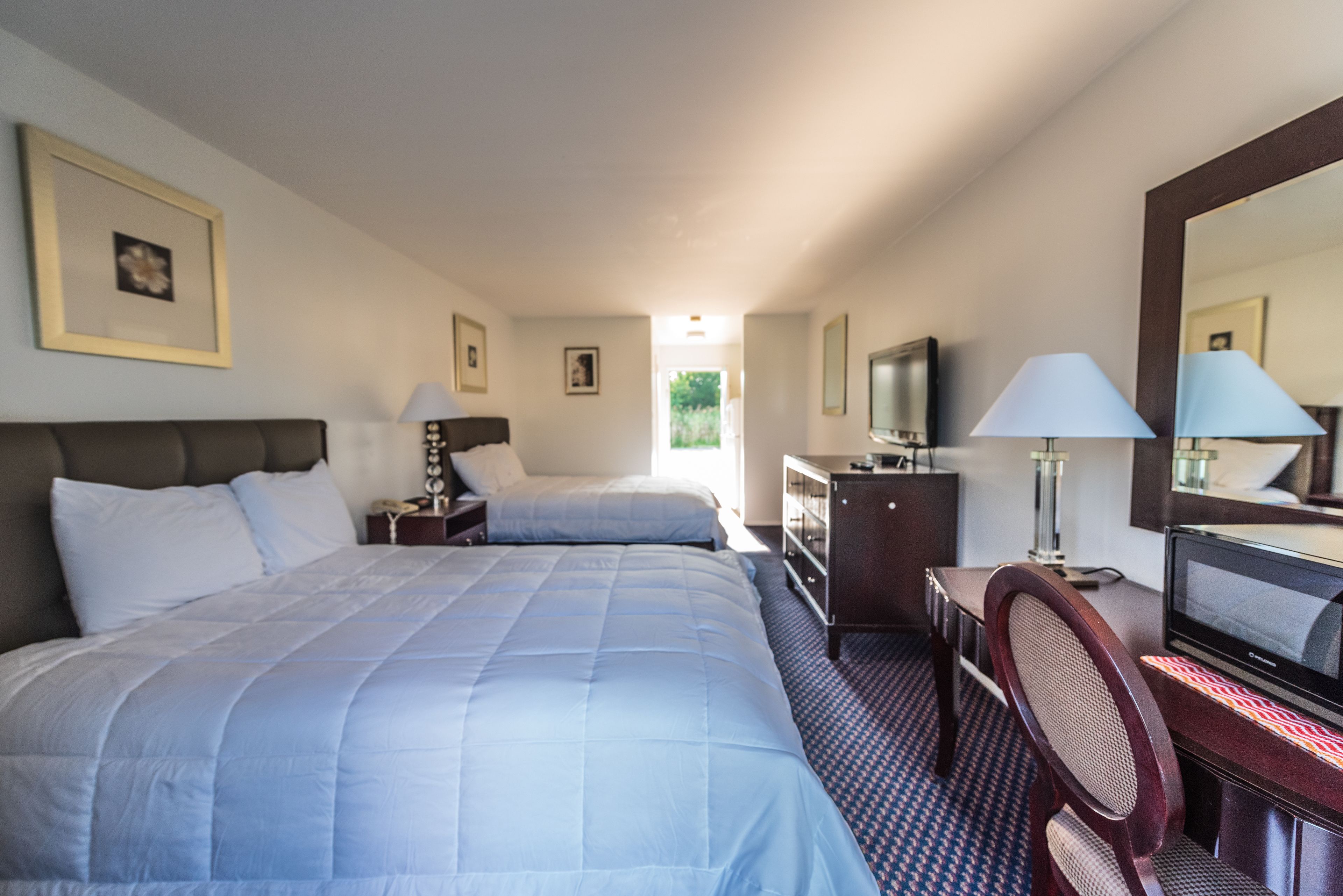 A hotel room with two beds, a desk with a chair, a television, and a dresser.