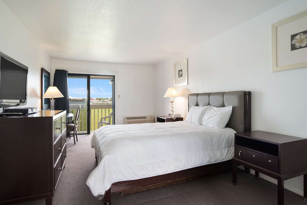 Habitación de hotel con cama, mesitas de noche, escritorio con silla, televisión y balcón con vistas.