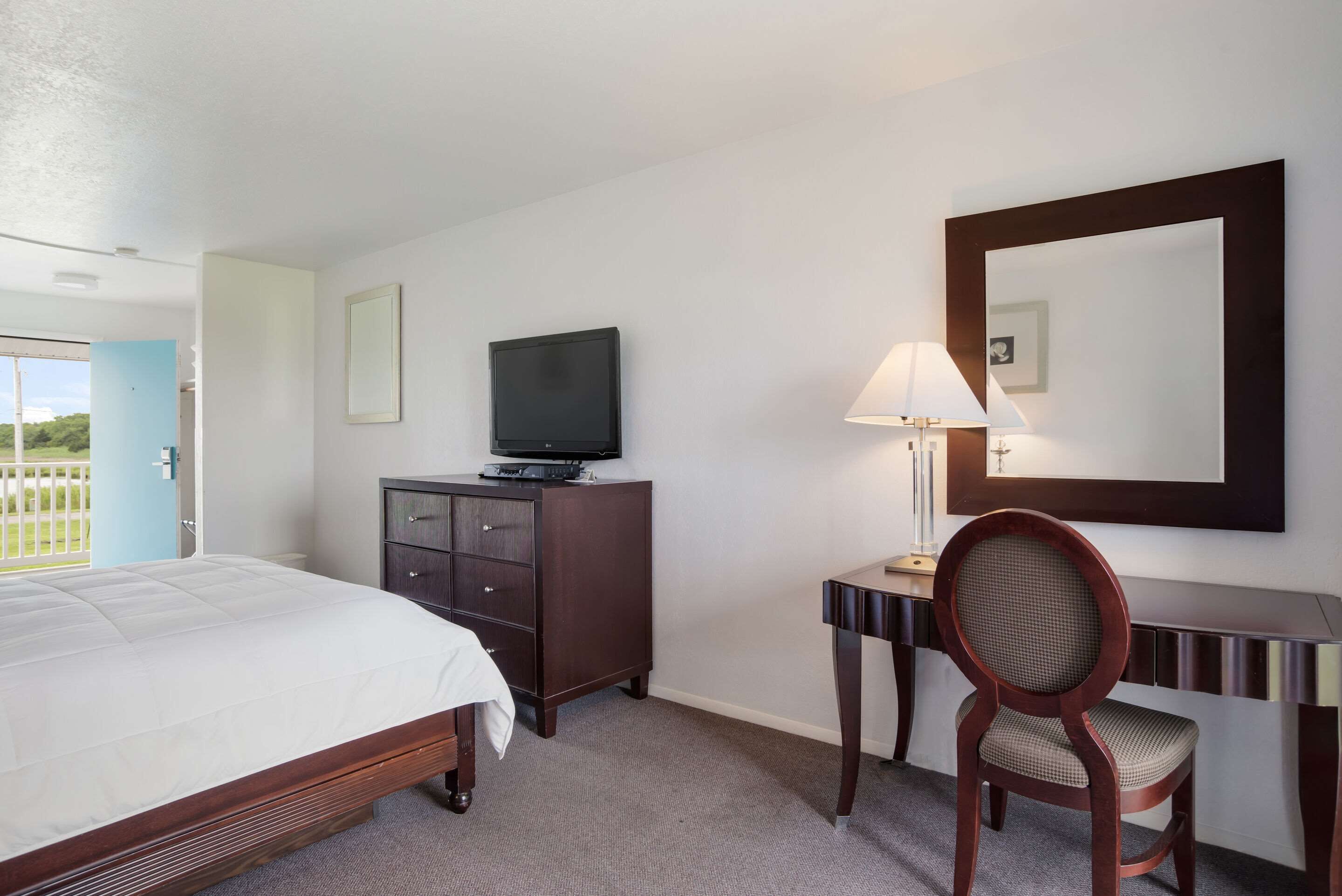 Ein Hotelzimmer mit Bett, Fernseher auf einer Kommode, Schreibtisch mit Lampe und einem Sessel.