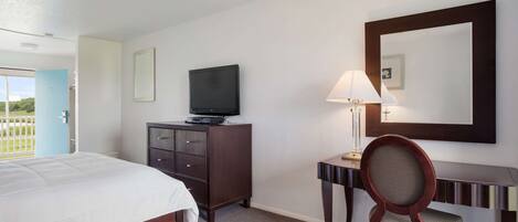 Habitación de hotel con cama, televisor en una cómoda, escritorio con lámpara y una silla.