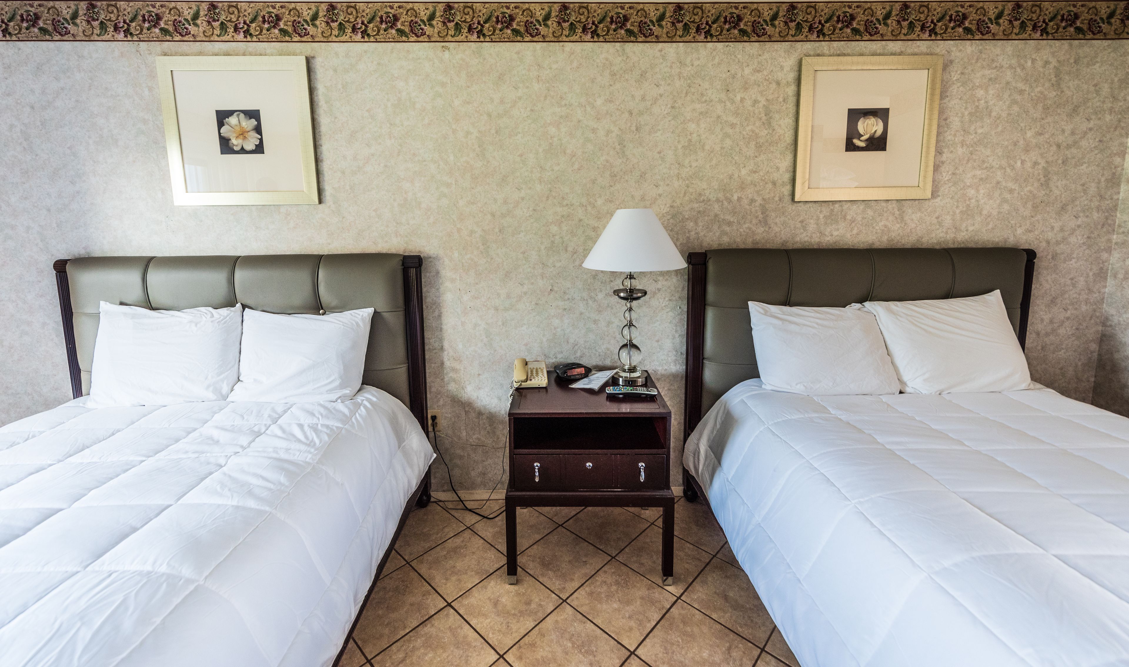 A hotel room with two beds, a nightstand with a lamp, and framed pictures on the wall.