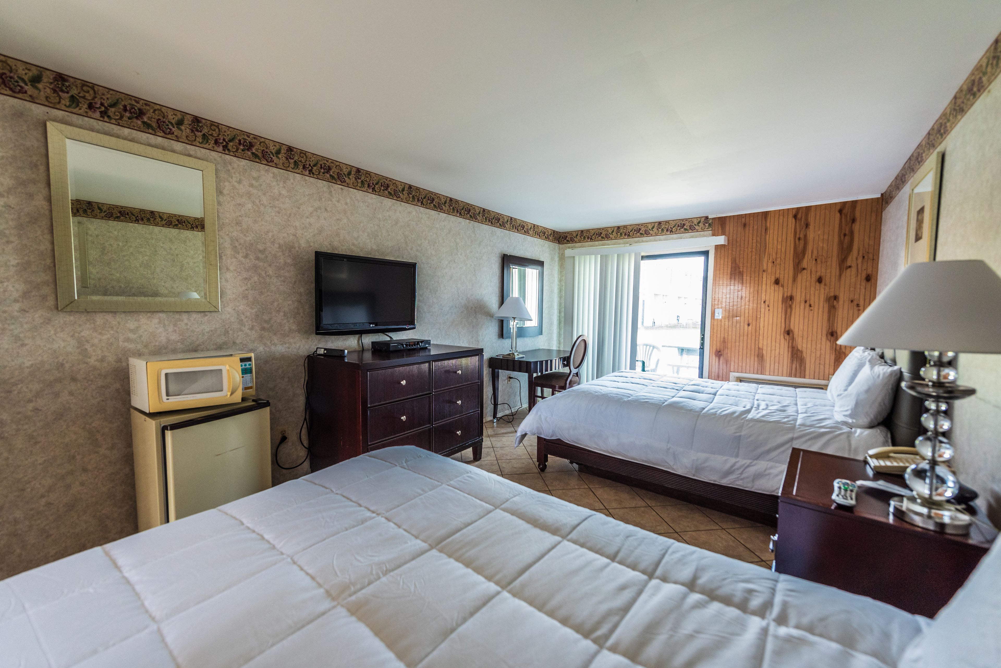 A hotel room with two beds, a television, a microwave, a desk with a lamp, and a mirror.
