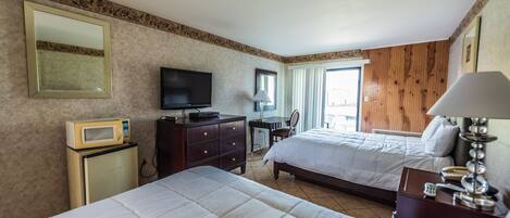 A hotel room with two beds, a television, a microwave, a desk with a lamp, and a mirror.