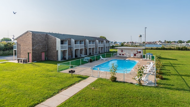 A hotel with a swimming pool, outdoor seating, and a view of the water. - Rodeway Inn at Somers Cove Marina (Crisfield)