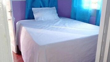 A single bed with white bedding in a room with purple walls and a blue headboard.