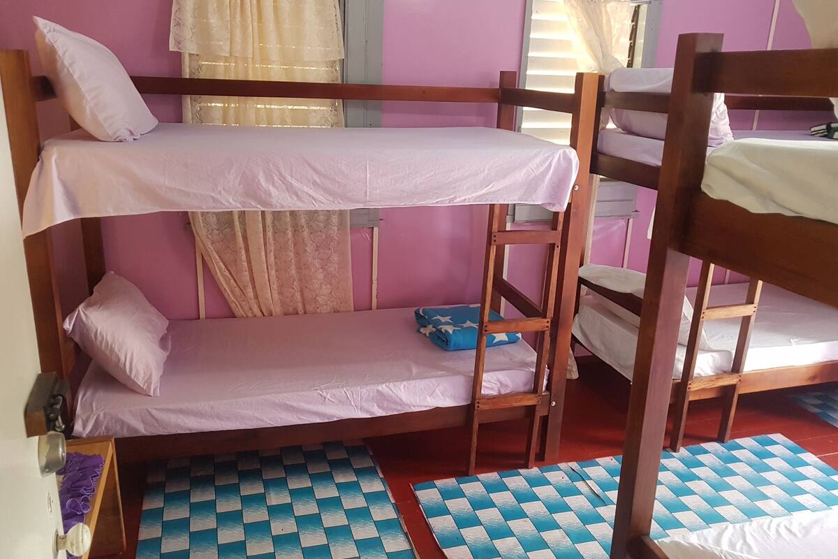 Une chambre avec un lit superposé, un sol à carreaux, une fenêtre avec des rideaux et une échelle en bois.