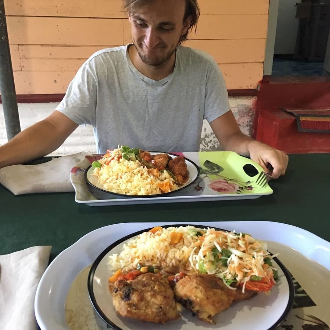A person seated at a table with two plates of food, one with rice and vegetables, and the other with meat and vegetables.