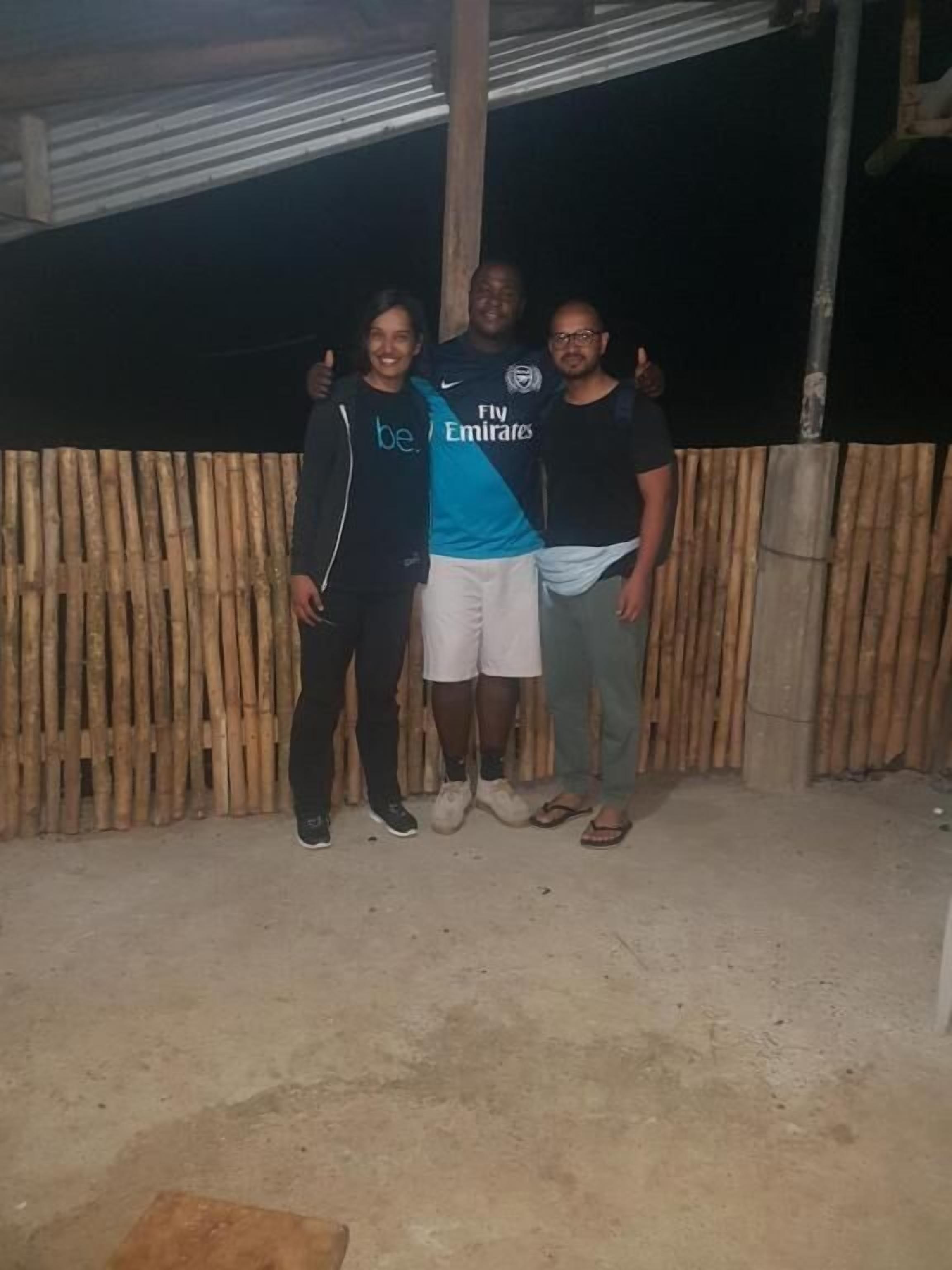 Three people standing in front of a bamboo fence.
